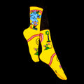 Lifestyle shot: Model wearing yellow Skate Day socks and black pants against a black background. [lf]