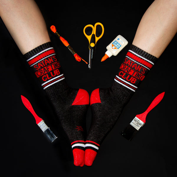 Lifestyle shot of a pair of Satan's Crafting Club socks worn with crafting supplies arranged around them. [lf]