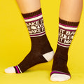 Lifestyle shot of a person wearing the 'Bake It Til You Make It' crew socks against a yellow background. [lf]