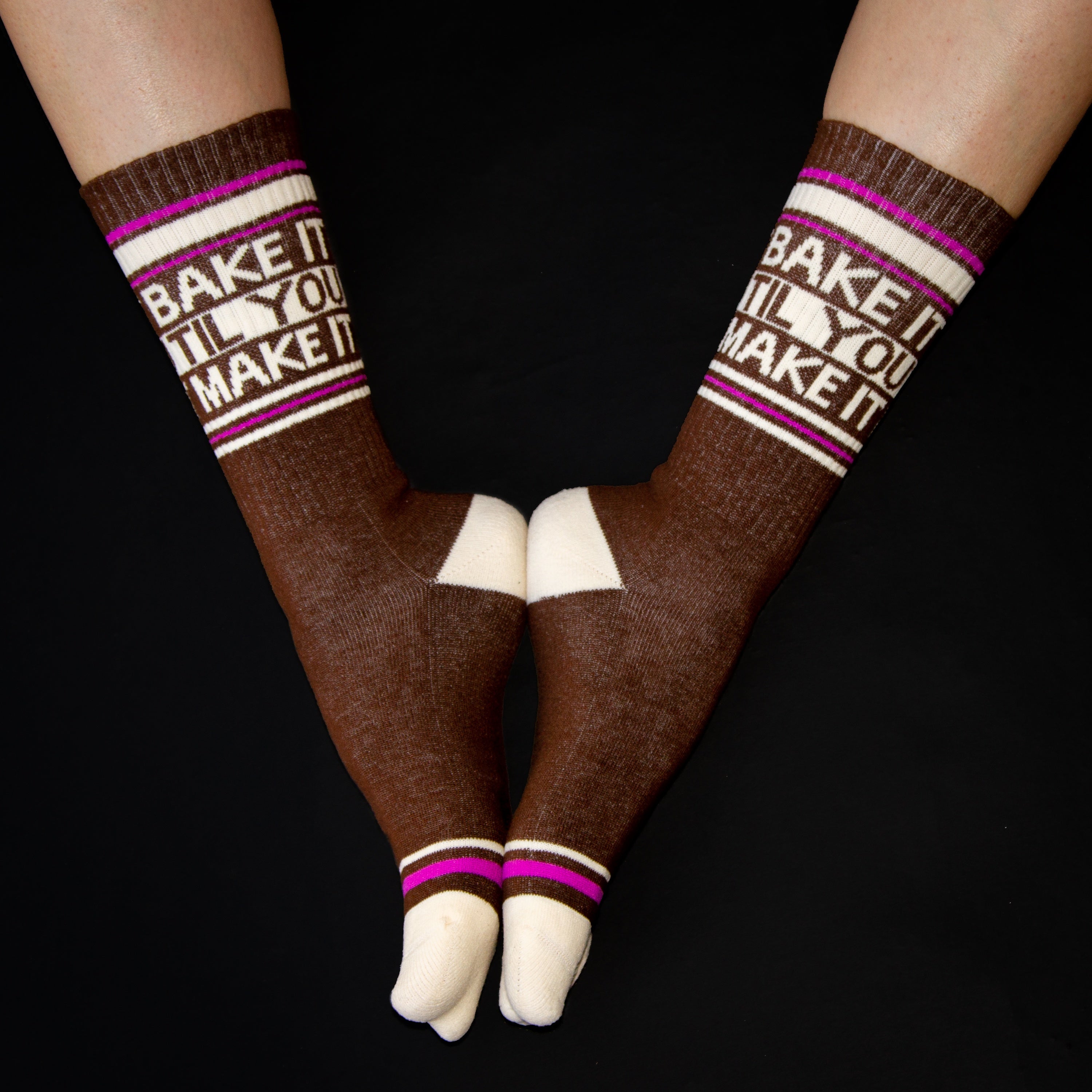 Flat lay shot of a pair of 'Bake It Til You Make It' crew socks against a black background. [lf]