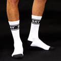 Studio shot of a person's legs showing the white crew socks with black 'GAY' band against a black background. [lf]