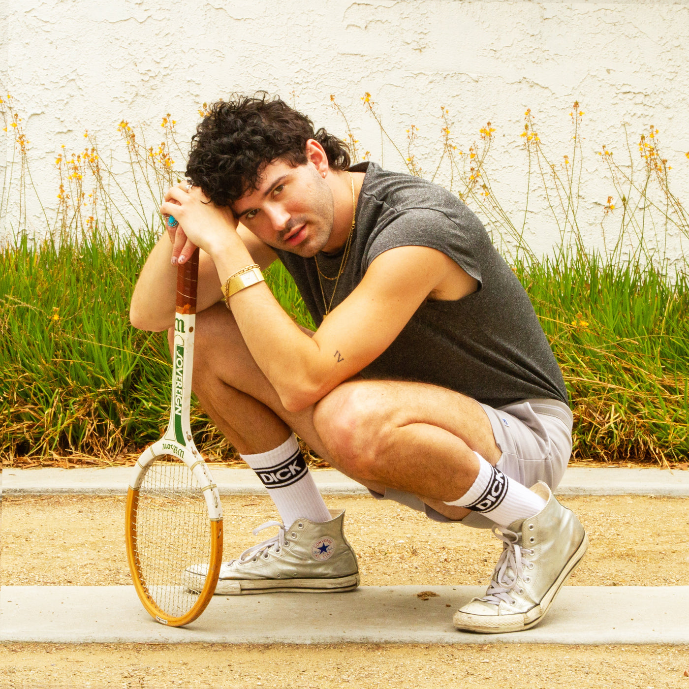 Lifestyle shot: A person wearing the 'Dick' socks and silver Converse sneakers, holding a tennis racket. [lf]