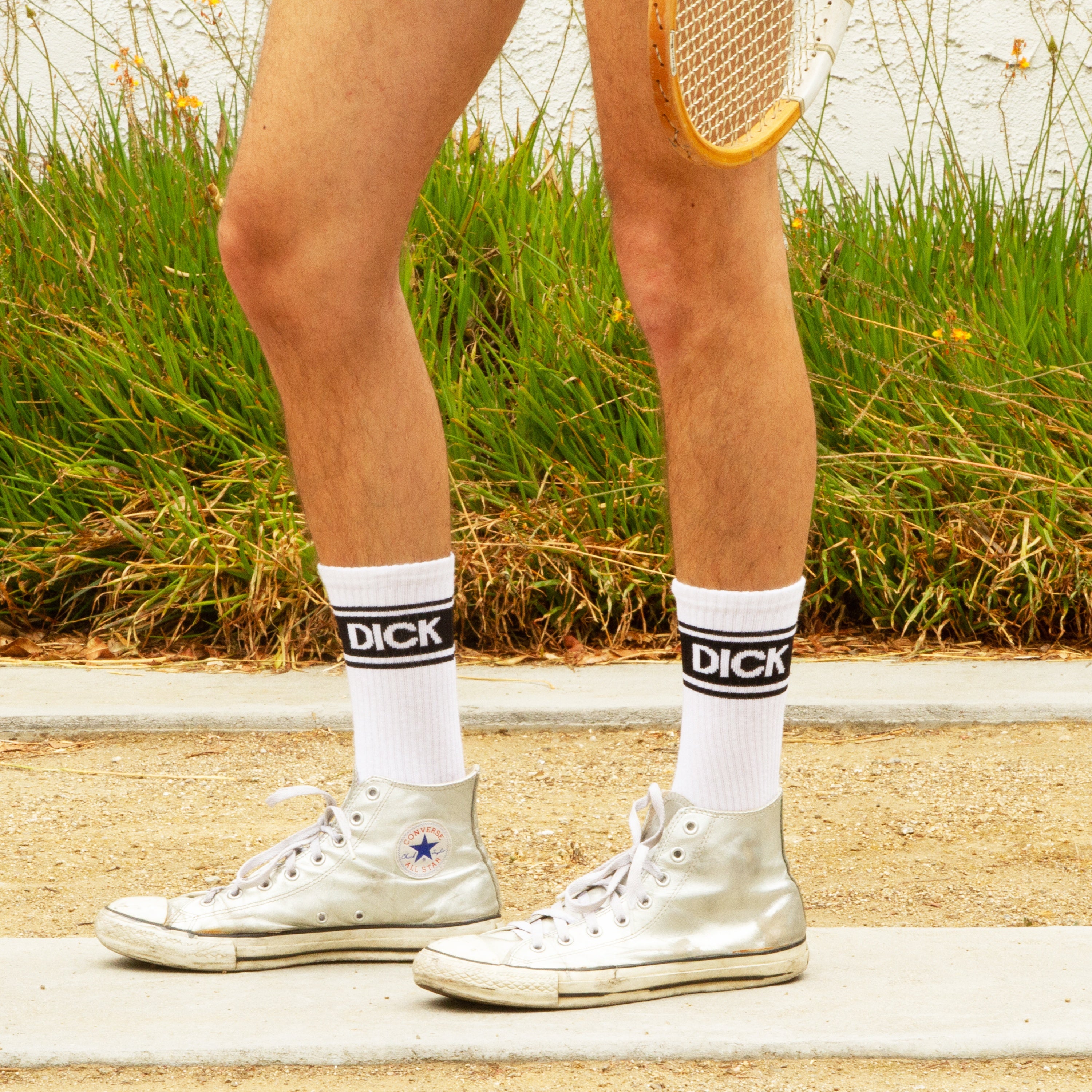 Lifestyle shot: Close-up of legs wearing 'Dick' socks and silver Converse sneakers. [lf]
