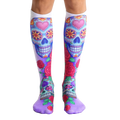 Pair of knee-high socks.  The main design features colorful sugar skulls with pink hearts and roses on a white and purple background. [lf]