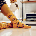 Lifestyle photo of a person wearing the pancake socks; syrup is being poured from a small pitcher onto the socks. [lf]