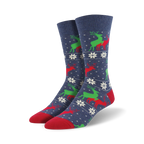 A pair of navy blue crew socks with a repeating pattern of red and green reindeer and white snowflakes. The socks have red toes and heels.