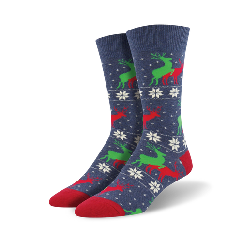 A pair of navy blue crew socks with a repeating pattern of red and green reindeer and white snowflakes. The socks have red toes and heels.