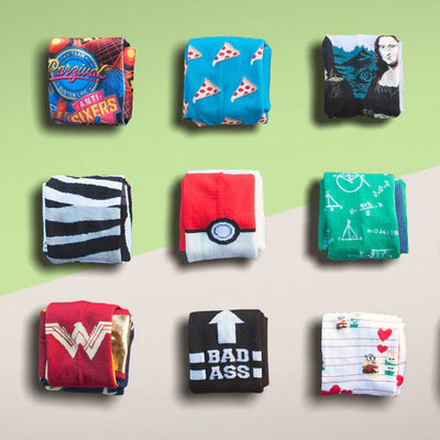 A flatlay showing folded pairs of women's crew socks in various designs: pizza, zebra, Pokémon, math, Mona Lisa, Wonder Woman, 'Bad Ass' arrow, and Minions.